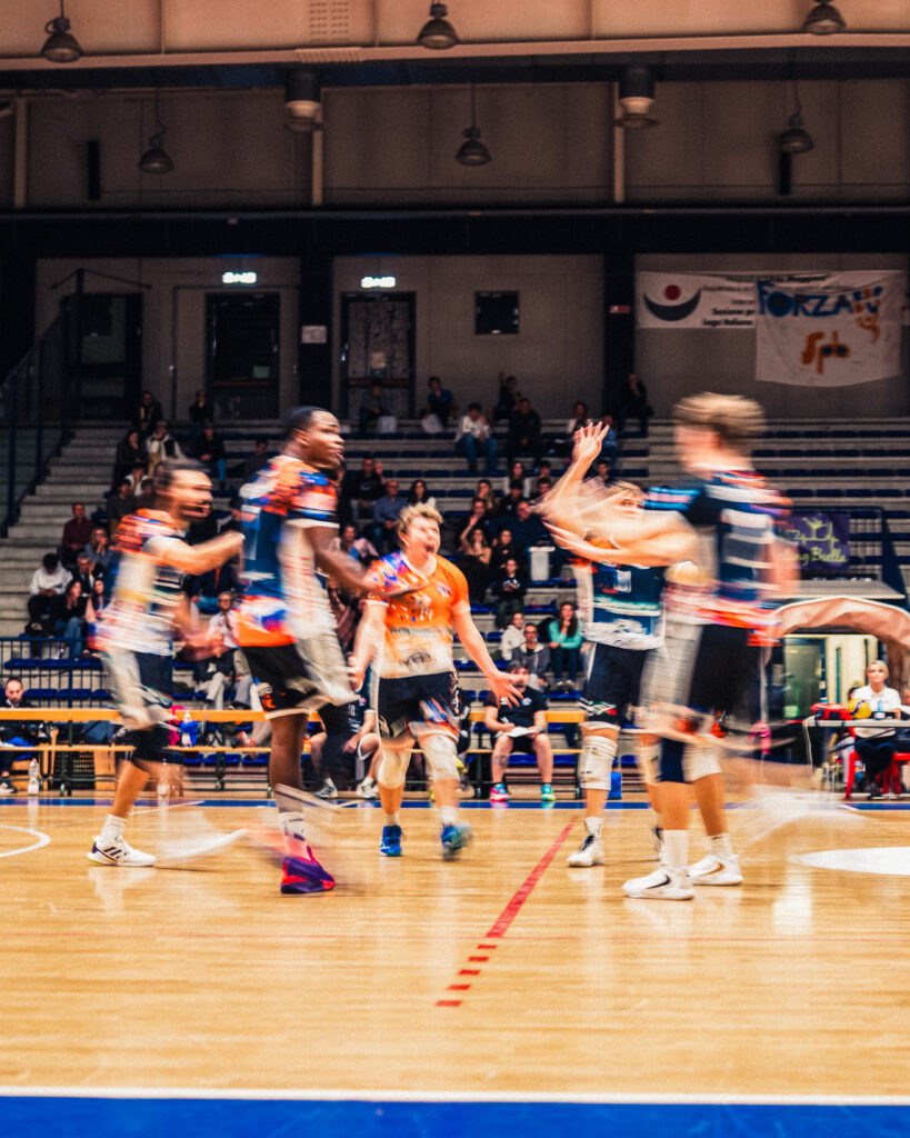Pallavolisti della serie B di Scuola Pallavolo Biellese in campo, in movimento in azione al Pala Pajetta di Biella, sullo sfondo gli spalti con tifosi